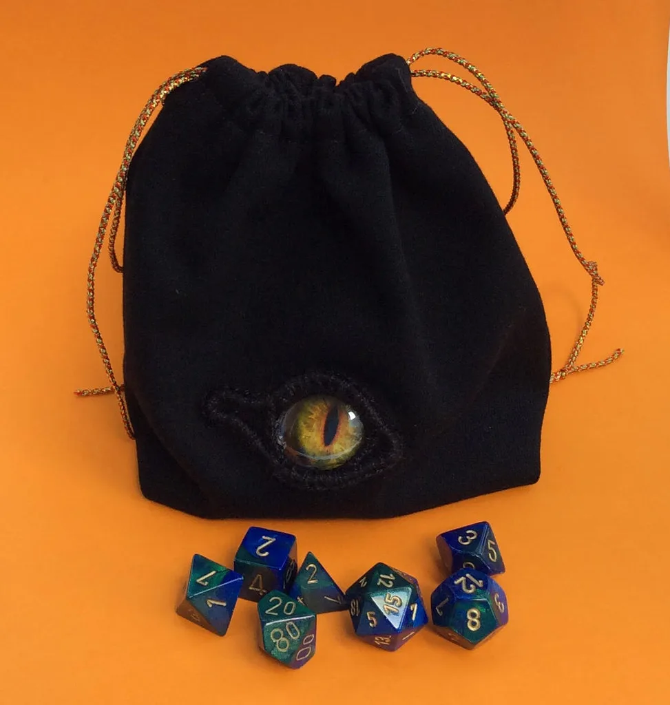 Pochette en tissu noir brodée d'un œil de dragon doré, exemple de broderie sur fond foncé