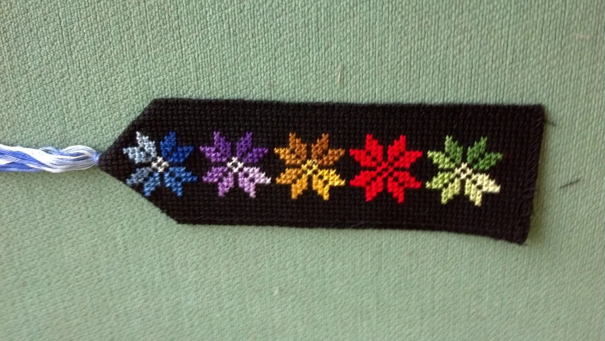Marque-page brodé au point de croix sur toile noire avec cinq étoiles florales bleue, violette, orange, rouge et verte