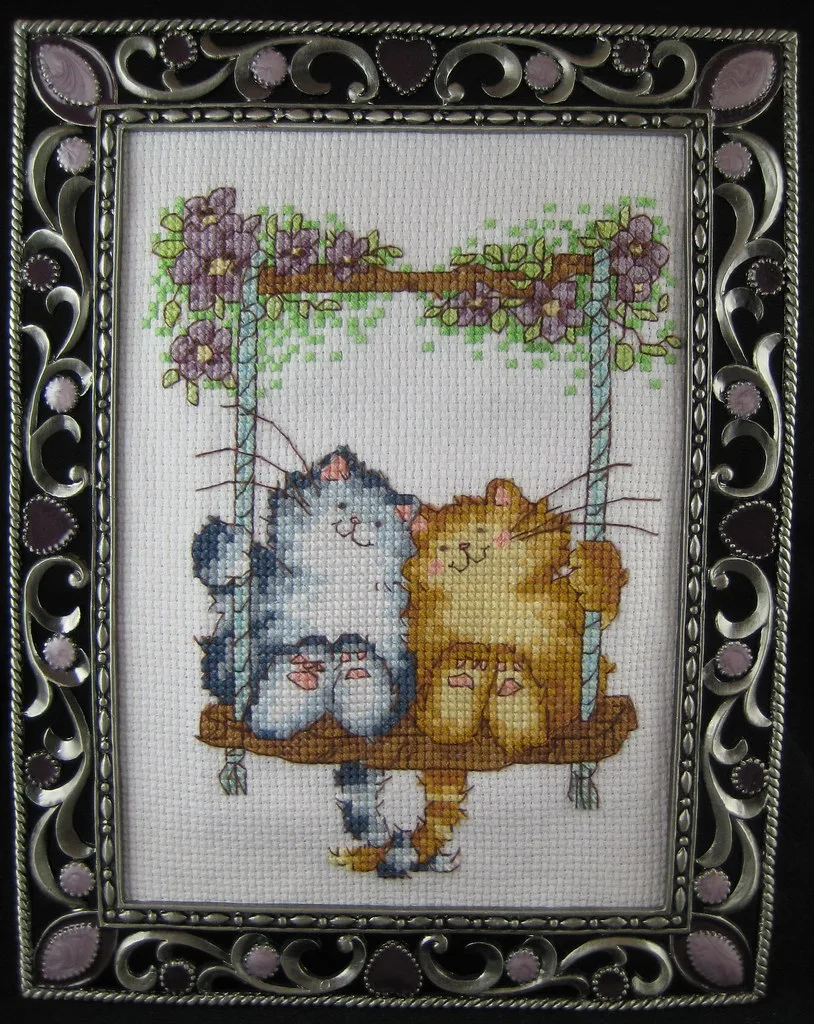 Broderie point de croix encadrée représentant deux chats sur une balançoire fleurie
