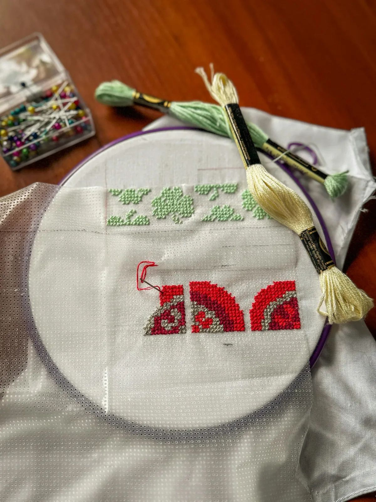 Fils DMC rouge et écheveaux disposés près d'un cerceau de broderie en cours, matériel pour débuter la broderie Assisi