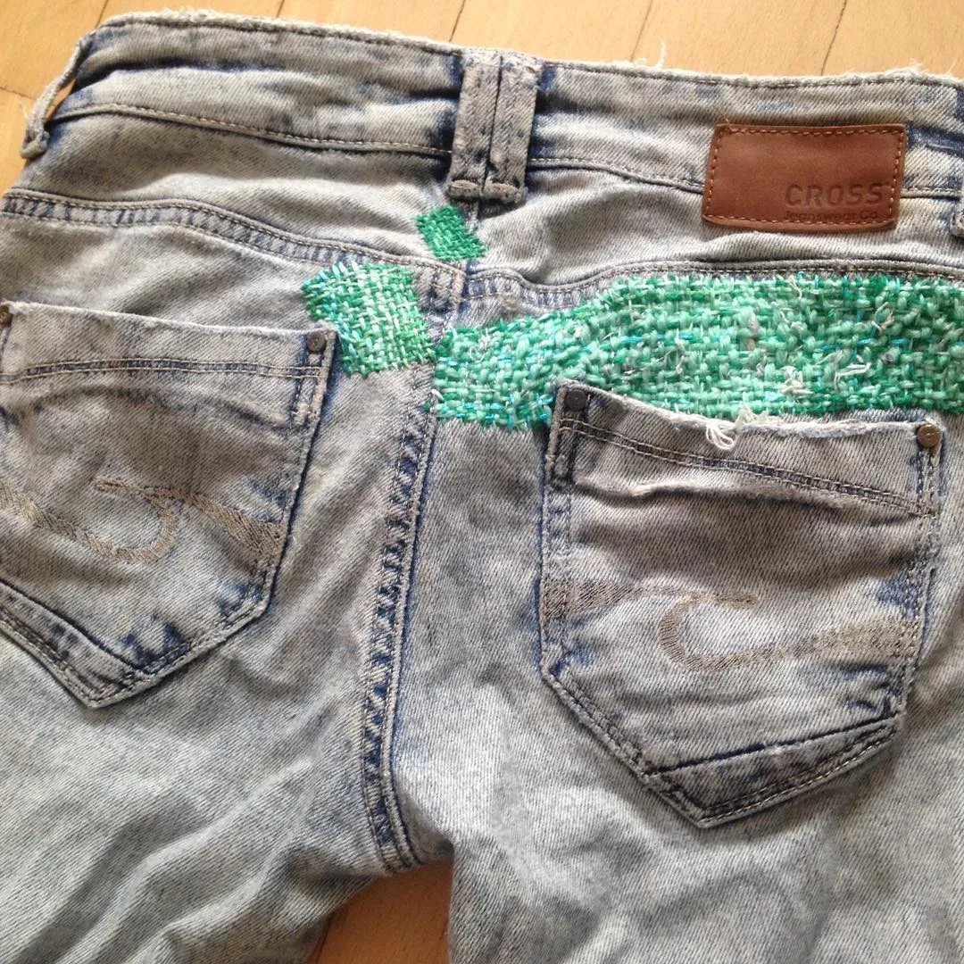 Poche arrière de jean avec une étiquette en cuir véritable et une reprise visible brodée en fil vert, exemple d'association du cuir et de la broderie