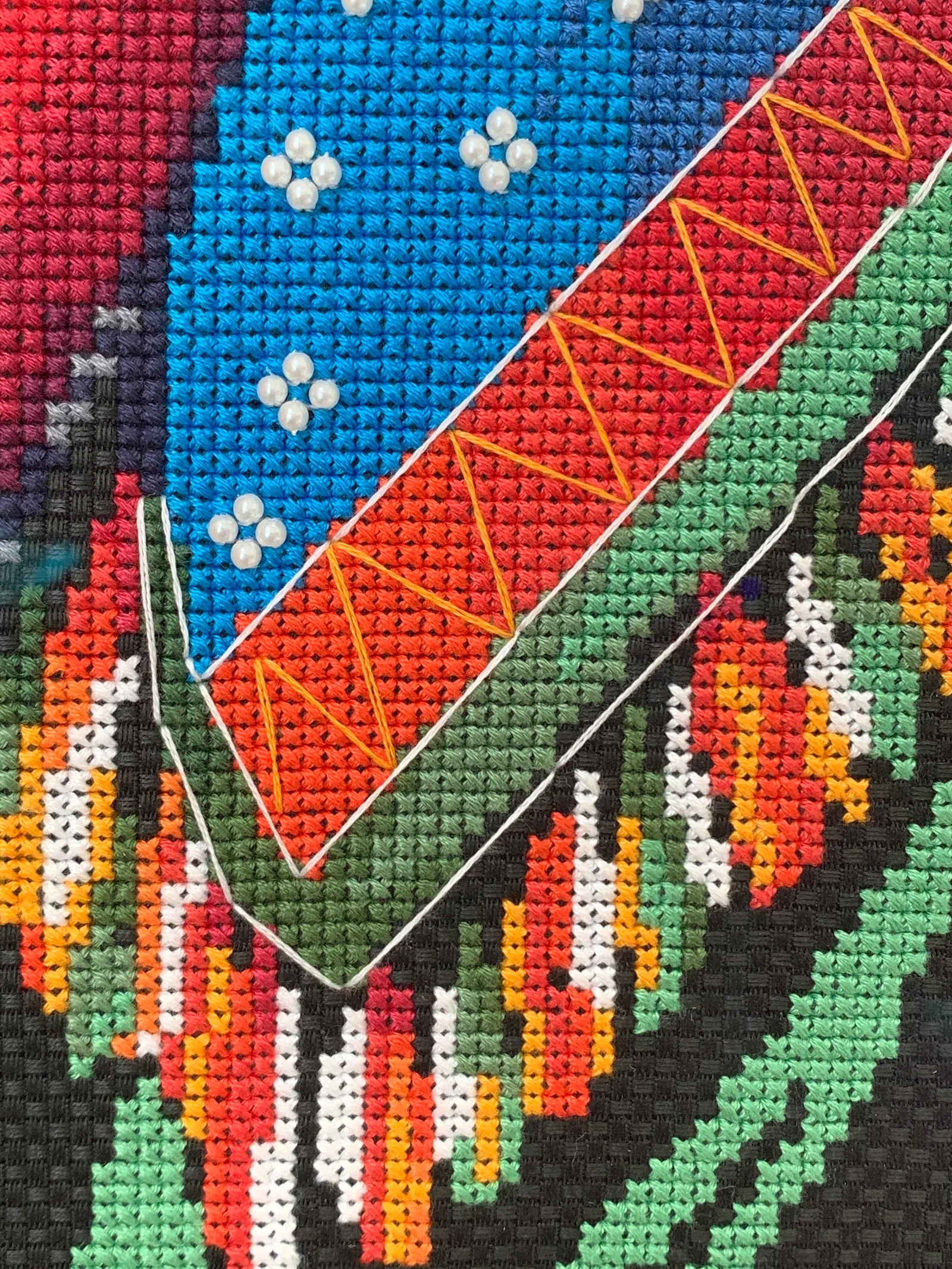Gros plan sur une broderie point de croix colorée aux motifs géométriques rouges et noirs, perles en relief