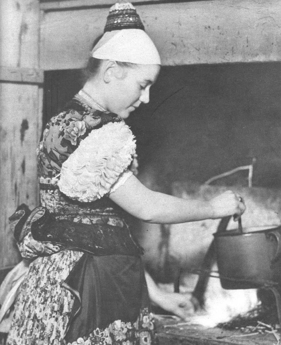 Photographie ancienne d'une femme en costume traditionnel hongrois brodé près d'un foyer