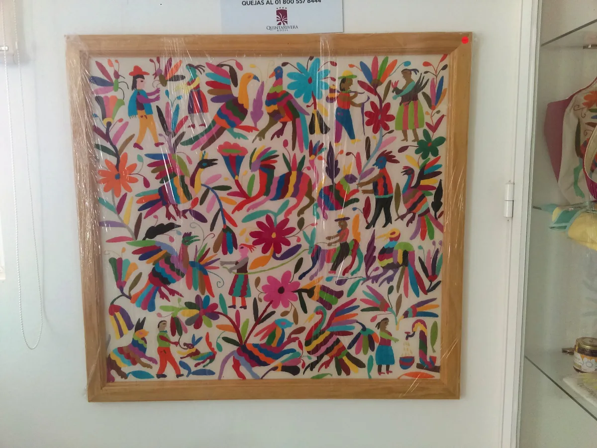 Broderie Otomi encadrée représentant une scène colorée d'animaux et de personnages sur fond blanc