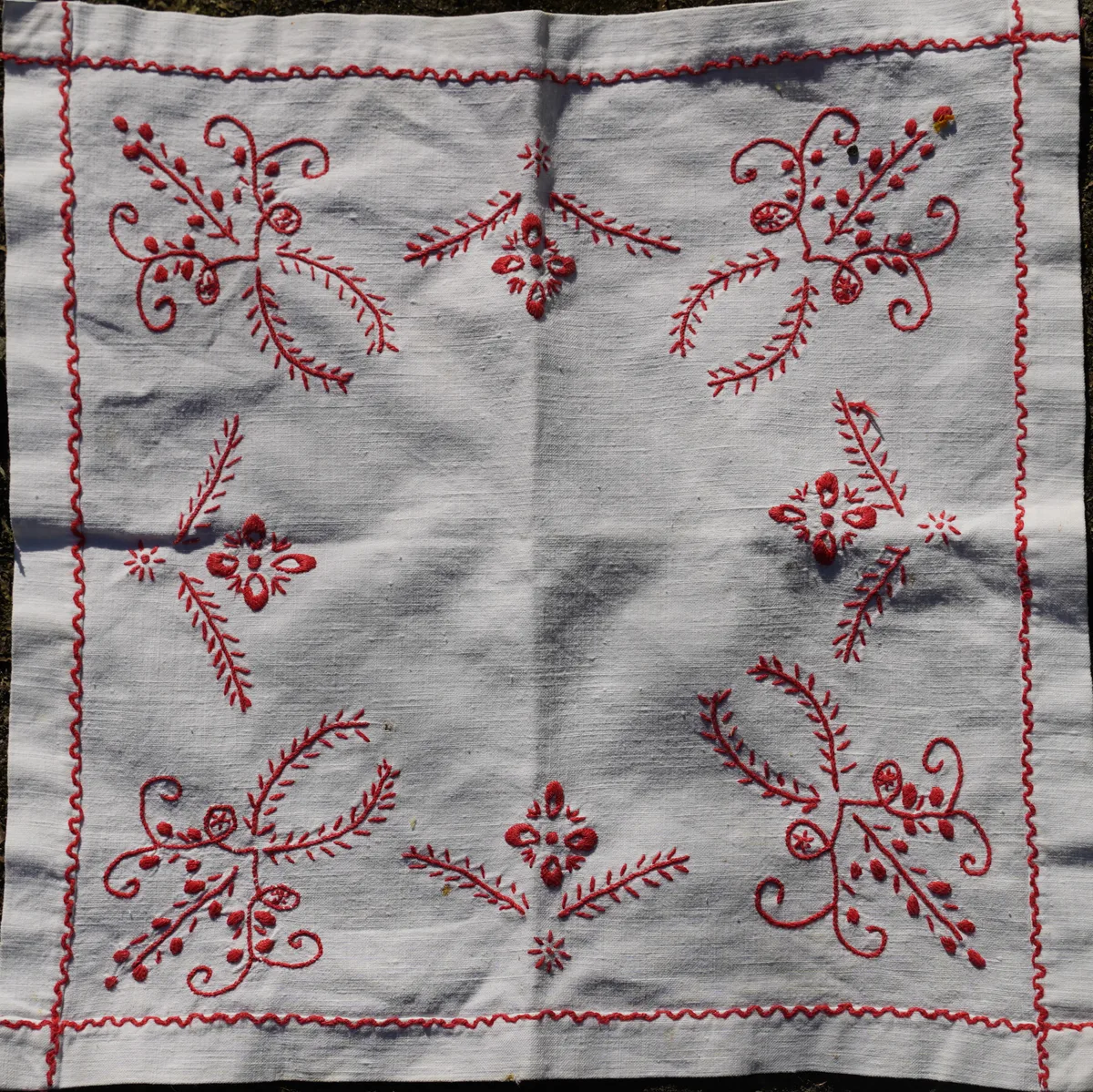 Détail d'une broderie traditionnelle portugaise de Guimarães en fil rouge sur lin blanc, motifs floraux symétriques