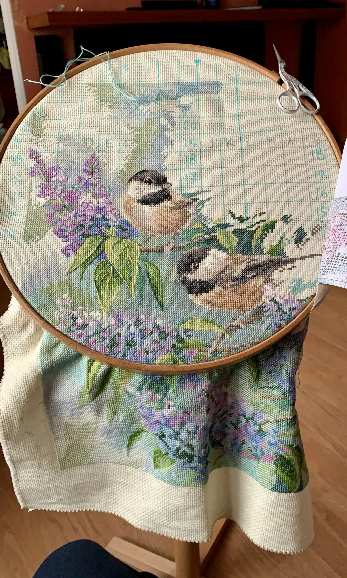 Broderie point de croix moderne représentant des oiseaux et fleurs, en cours de réalisation sur cerceau avec grille visible