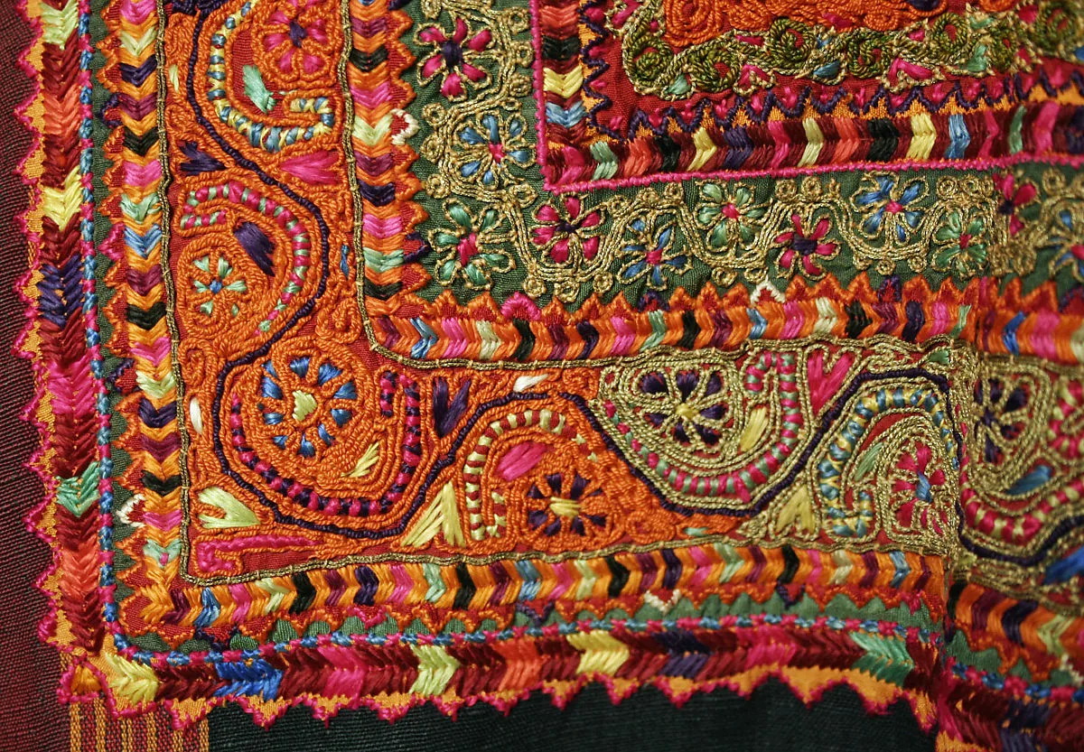 Détail de broderie traditionnelle richement colorée sur un vêtement ancien, motifs floraux et géométriques