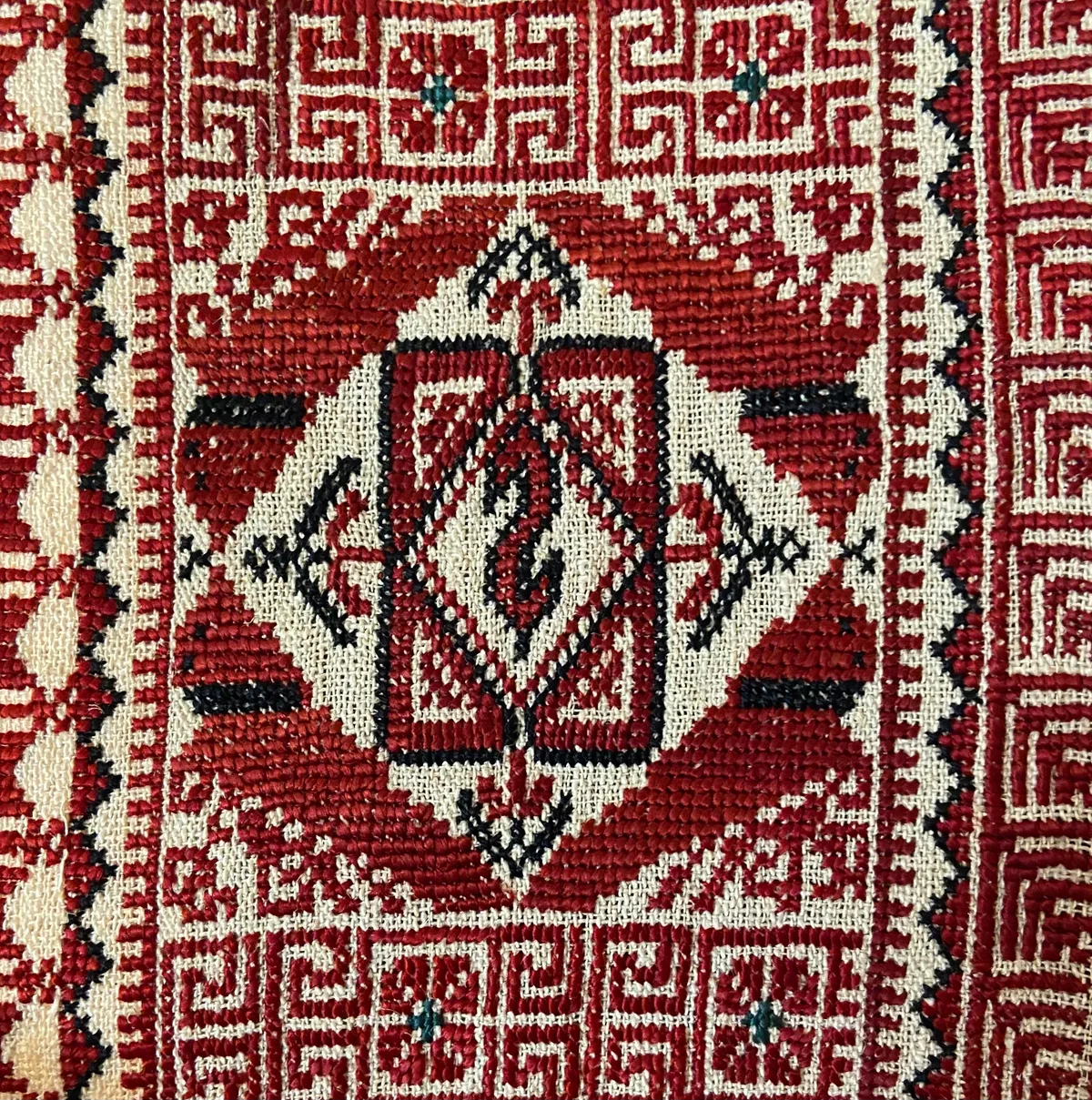 Détail macro d'une broderie tatreez palestinienne au point de croix, motifs géométriques rouge et crème