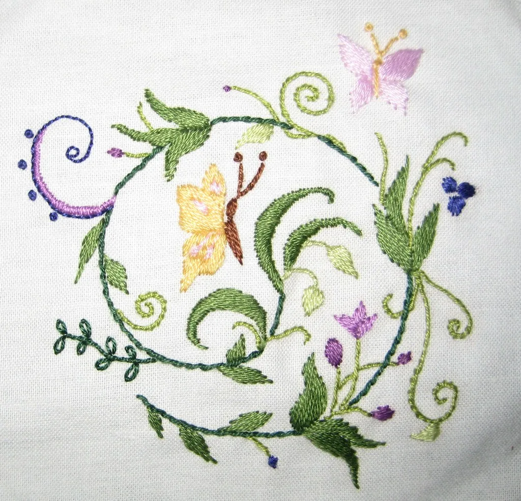 Broderie végétale avec motifs de feuilles, fleurs et papillons réalisée au point de croix sur toile blanche