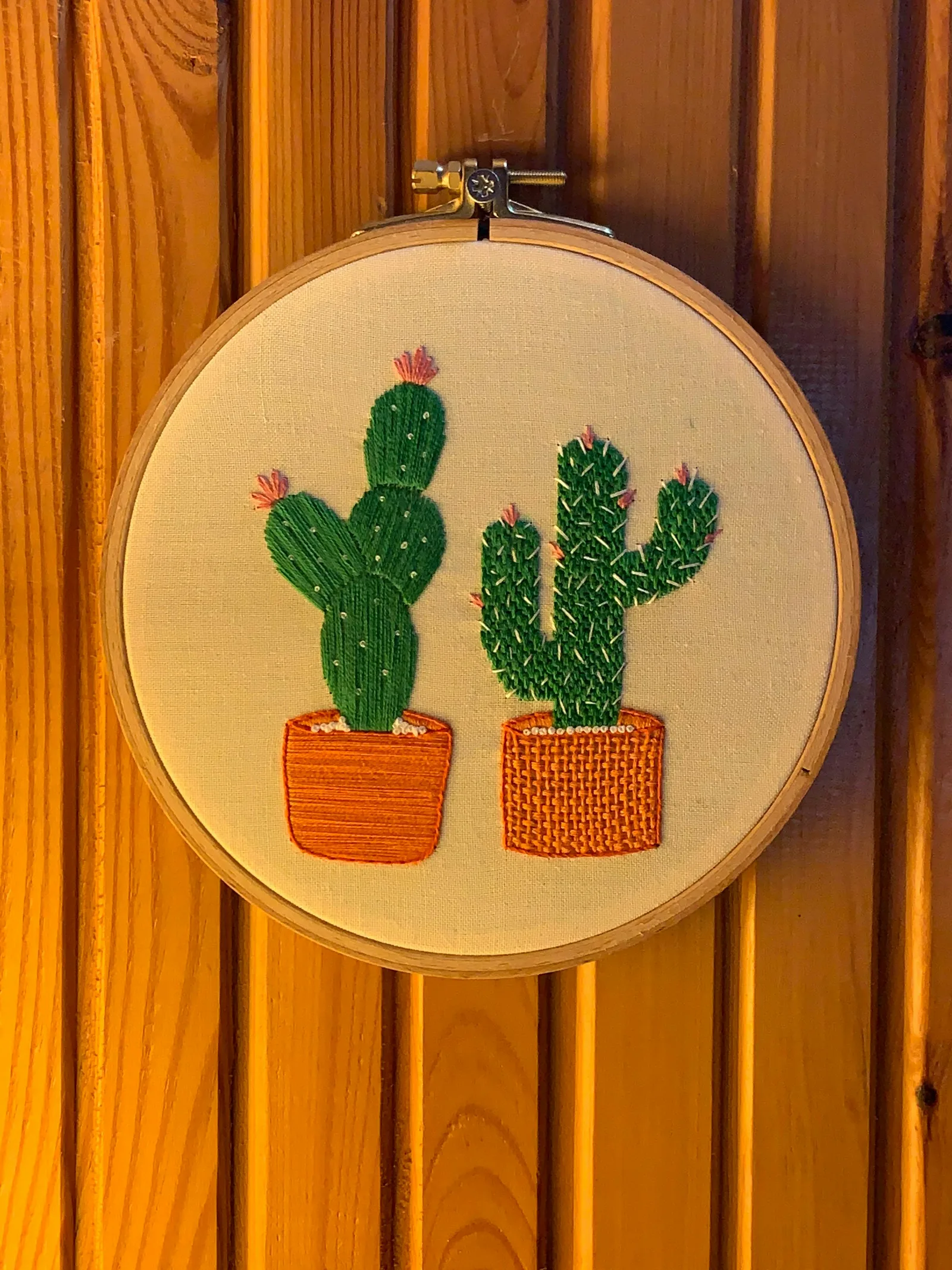 Broderie grand format encadrée d'un motif de cactus, accrochée sur un mur en bois dans un salon
