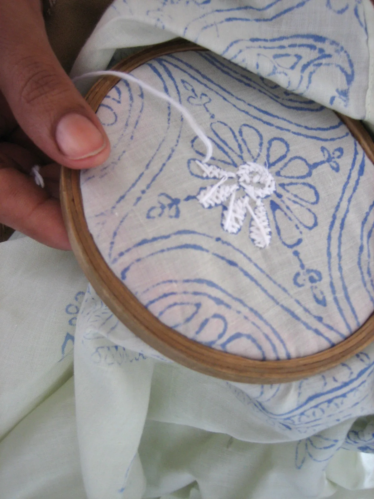 Main brodant un motif chikankari au point d'ombre sur un cerceau, technique bakhiya sur tissu à motifs bleus
