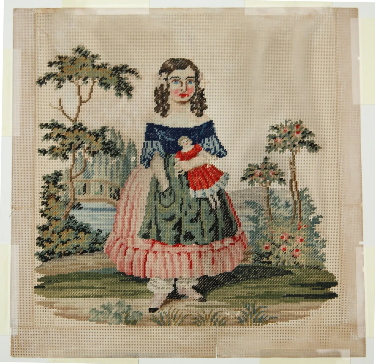 Broderie ancienne encadrée représentant une fillette tenant une poupée dans un jardin, style victorien