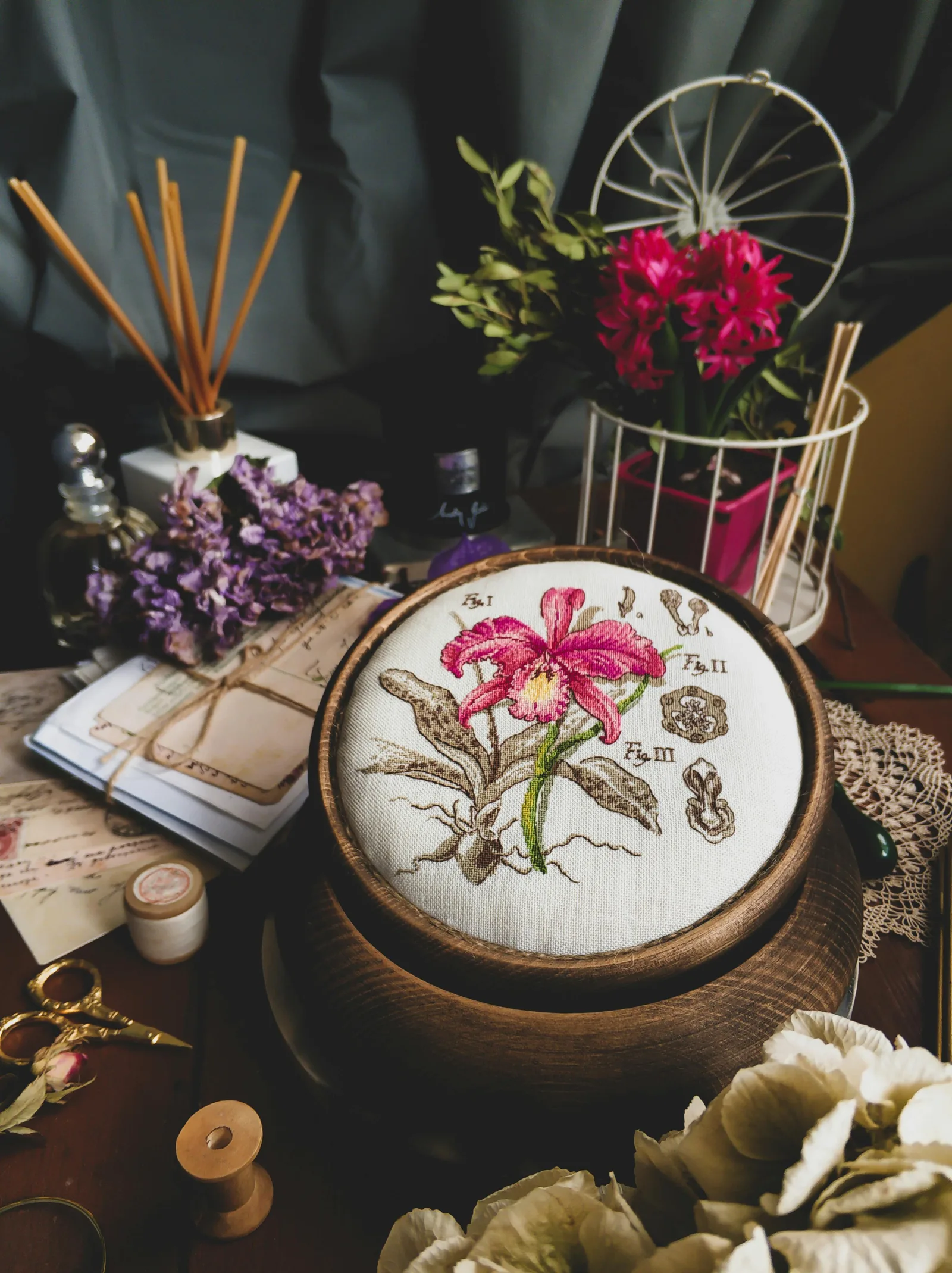 Cerceau de broderie botanique avec orchidée brodée en fil coloré sur tissu lin, entouré d'accessoires de couture vintage