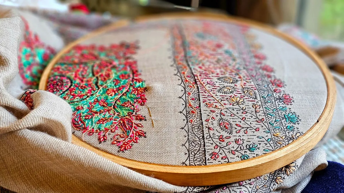 Gros plan sur une broderie colorée en cours de réalisation dans un cerceau en bois, aux motifs floraux détaillés
