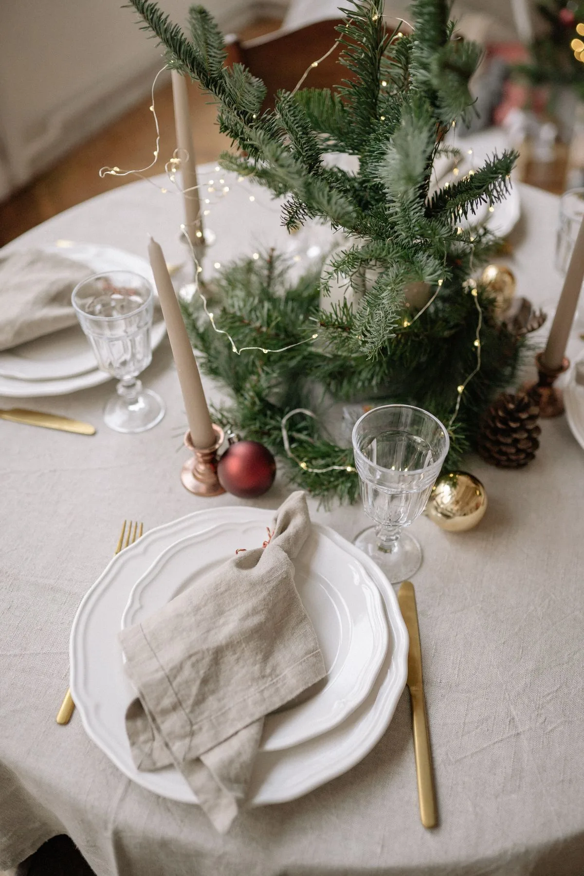 Table de Noël dressée avec nappe en lin, bougies, branches de sapin et serviette brodée dans une ambiance chaleureuse