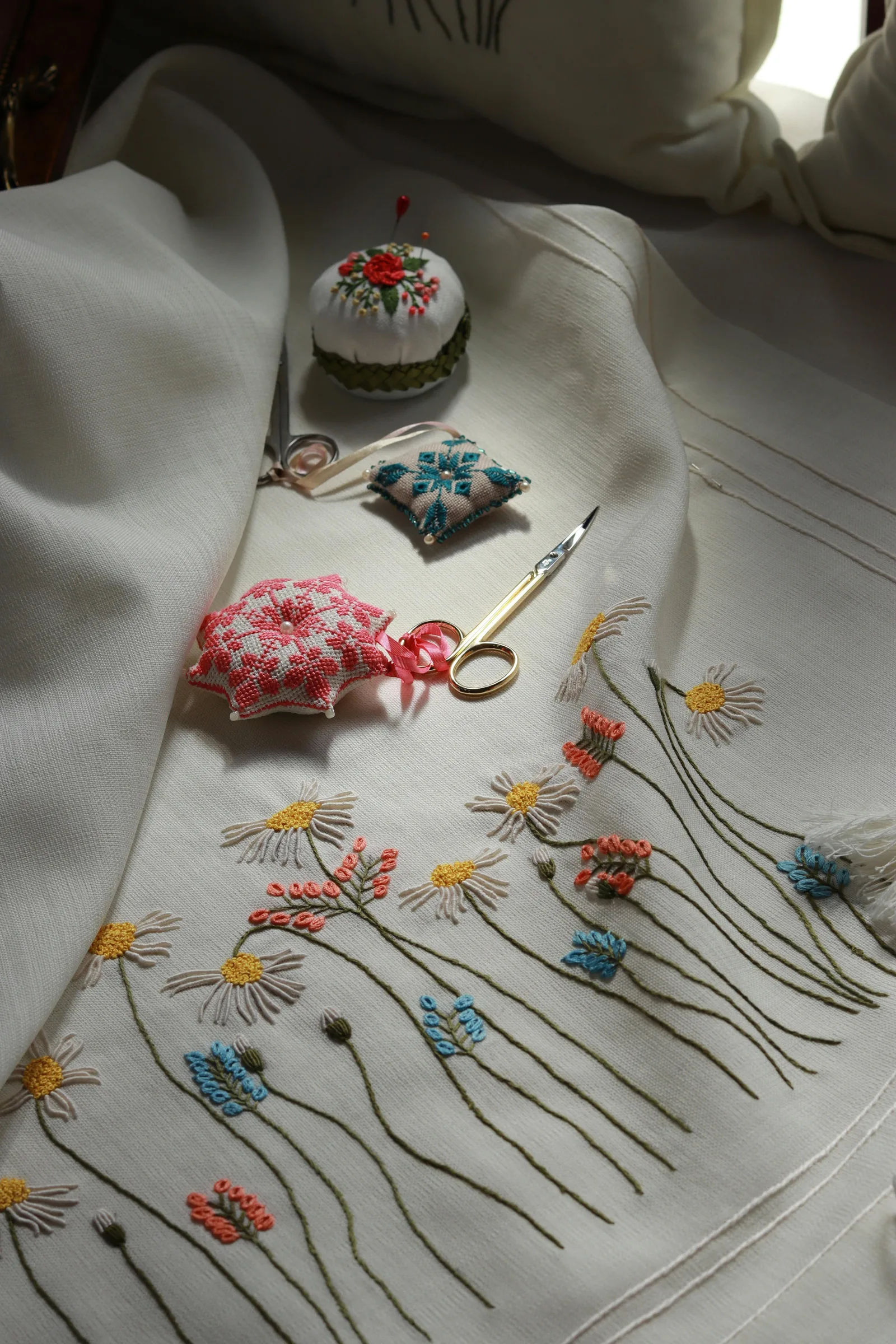 Table de travail en lin avec broderie, ciseaux et pelote d'épingles : poste de broderie dégagé pour une bonne posture