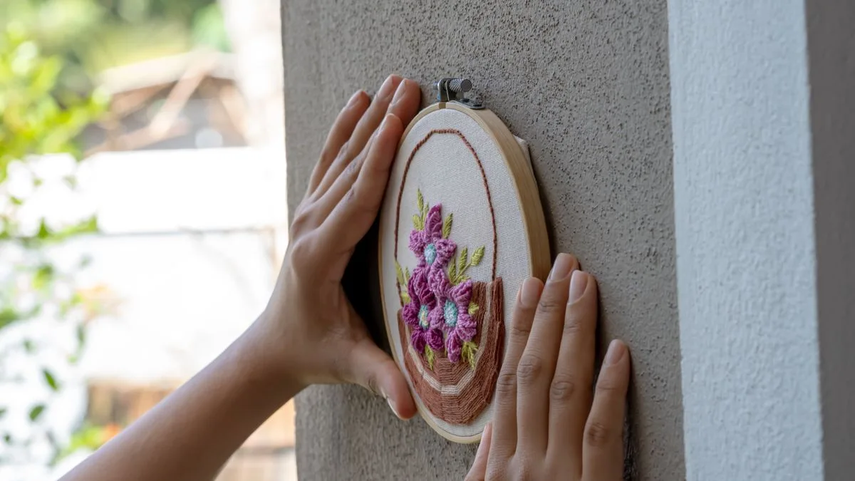Mains tenant et positionnant un cerceau brodé fleuri sur un mur pour l'accrocher en décoration