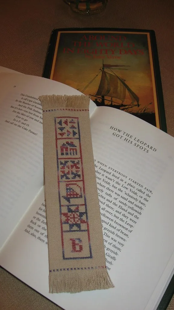 Marque-page brodé au point de croix sur lin avec une colonne de petits motifs géométriques posé sur un livre ouvert