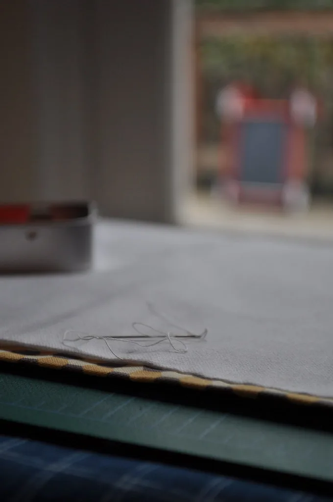 Ouvrage de broderie inachevé posé sur une table avec son aiguille encore enfilée et sa boîte en métal
