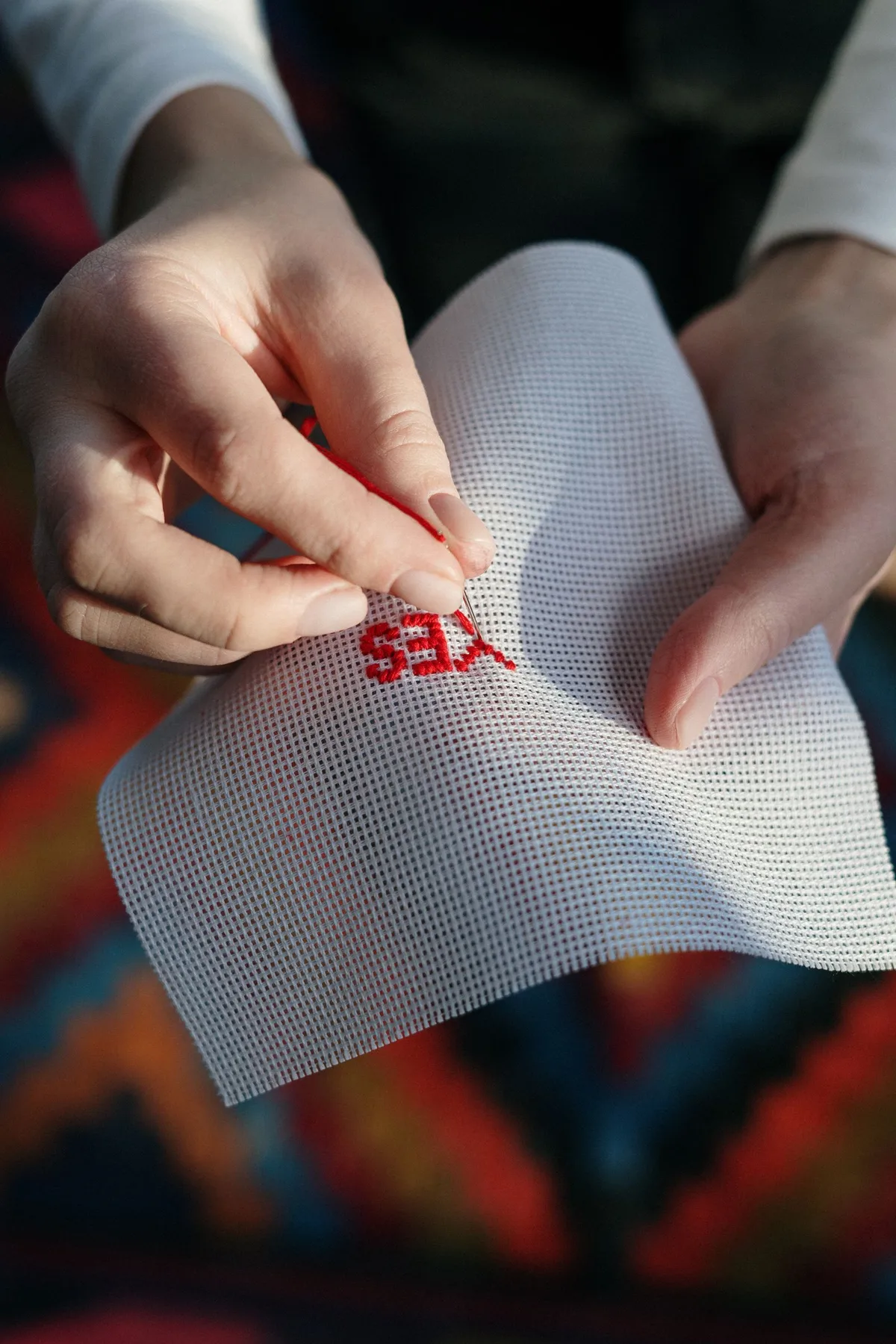 Gros plan sur des mains brodant un motif au point de croix avec un fil rouge sur toile Aida