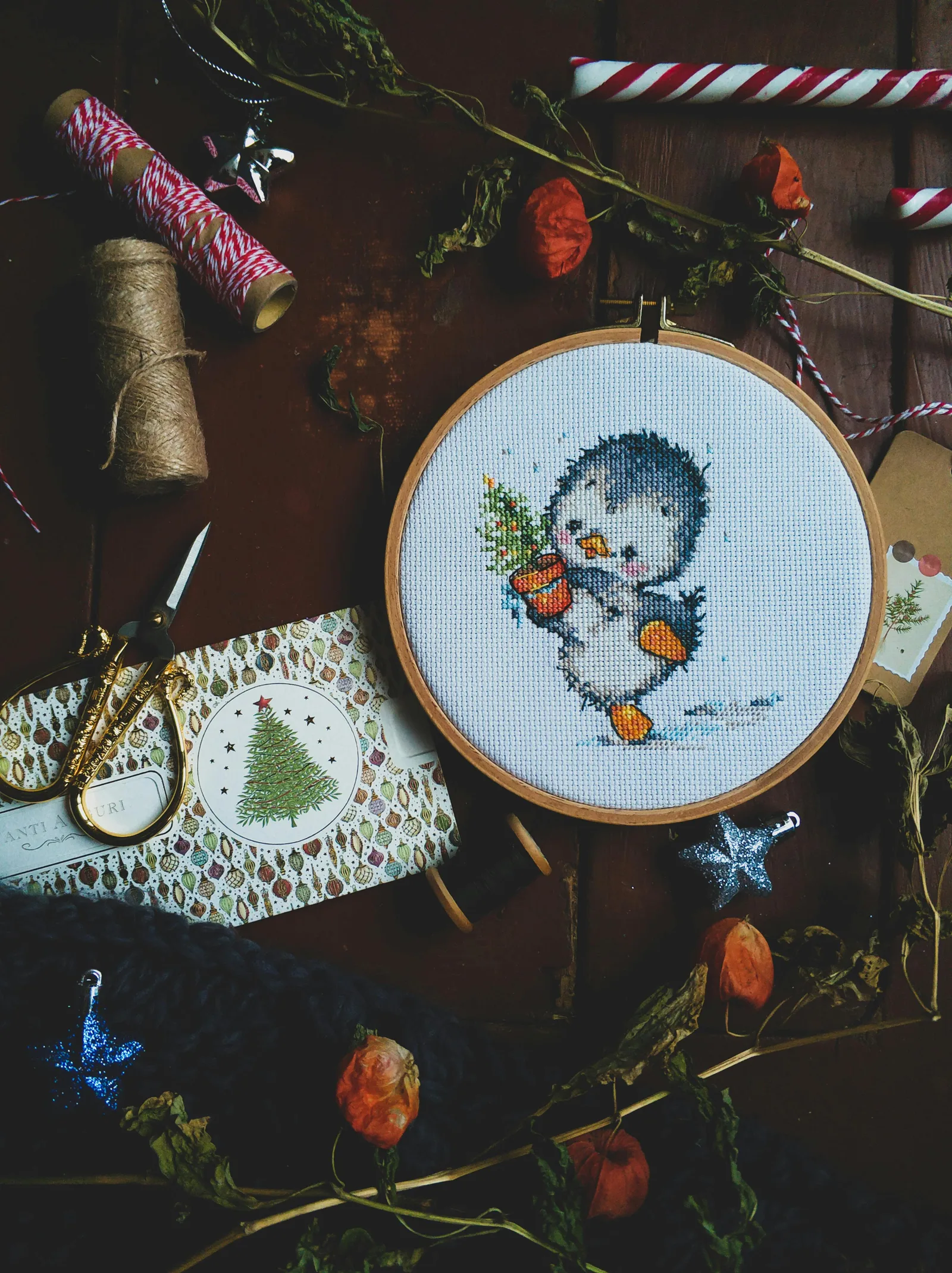 Broderie point de croix de Noël avec manchot dans un cerceau entouré de décorations festives et fils colorés