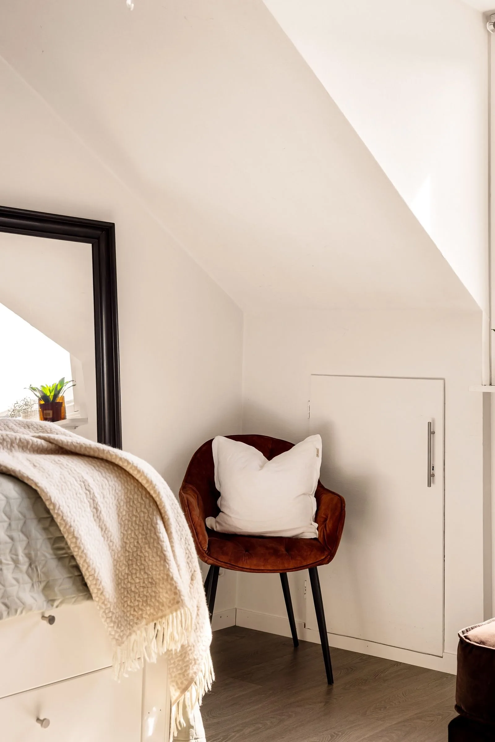 Coin salon moderne et épuré avec fauteuil en velours brique, coussin blanc et liseuse, décor minimaliste sous lucarne