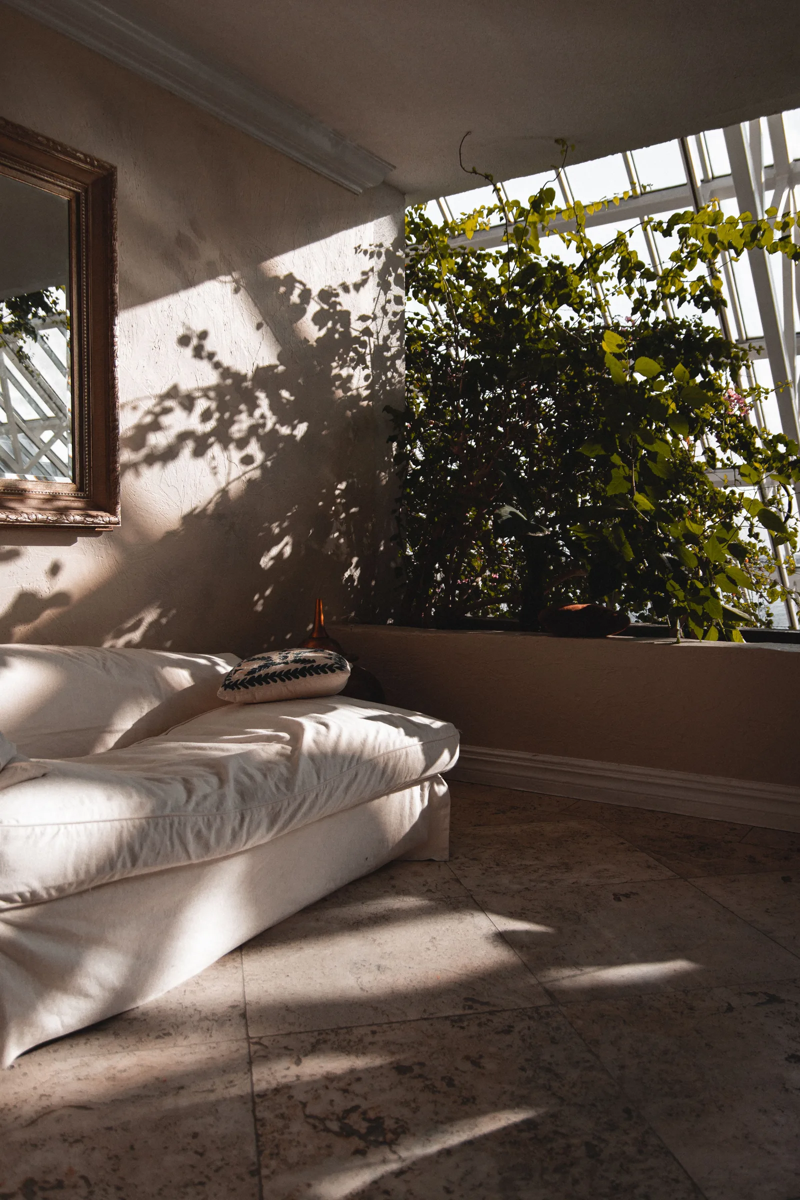 Salon estival lumineux avec grand canapé blanc et lumière naturelle filtrant à travers des plantes vertes, atmosphère légère et aérée propice aux textiles brodés