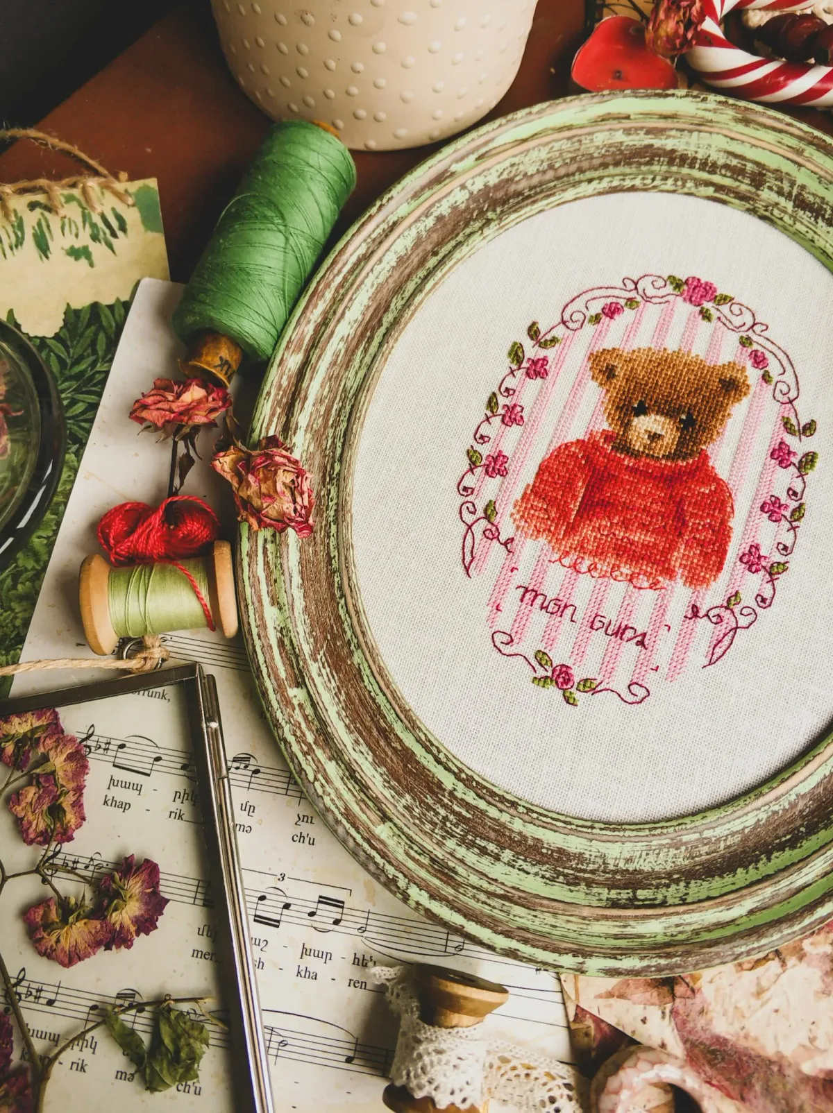 Broderie au point de croix d'un ourson au pull rouge dans un cadre ovale fleuri, ouvrage fini aux nombreuses nuances