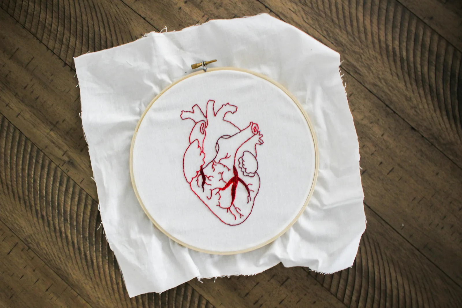 Petit cerceau de broderie en bois avec un cœur brodé au fil rouge posé sur un plancher, exemple de petit ouvrage adapté au cerceau