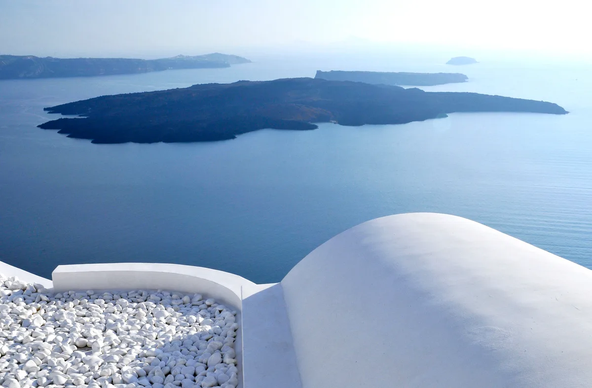 Vue sur la caldeira de Santorin depuis une terrasse en pierre blanche — architecture cycladique blanche et bleue, mer Égée en arrière-plan évoquant l'essence de la palette méditerranéenne
