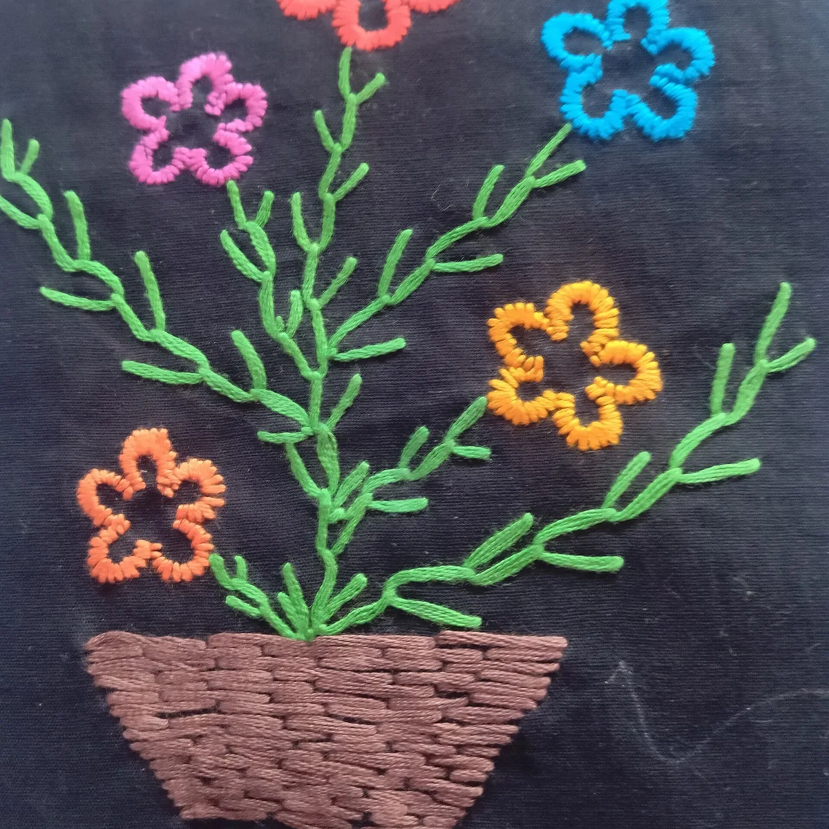 Pot de fleurs brodé sur toile noire, fleurs au point de feston, tiges au point de plume et pot au passé empiétant