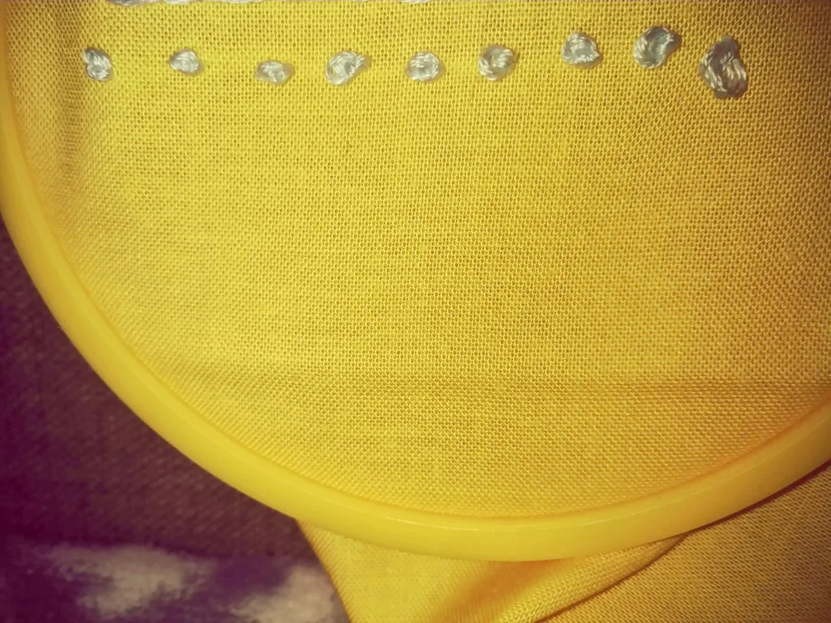 Toile jaune tendue dans un cerceau avec une ligne de nœuds français brodés au fil métallisé, exercice de points de broderie pour débutant