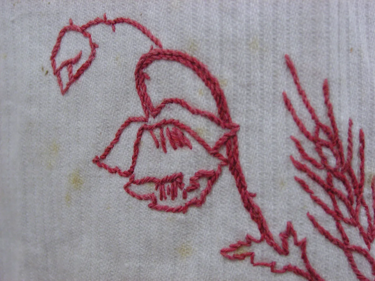 Détail macro d'un motif redwork brodé au point de tige en fil rouge sur toile blanche