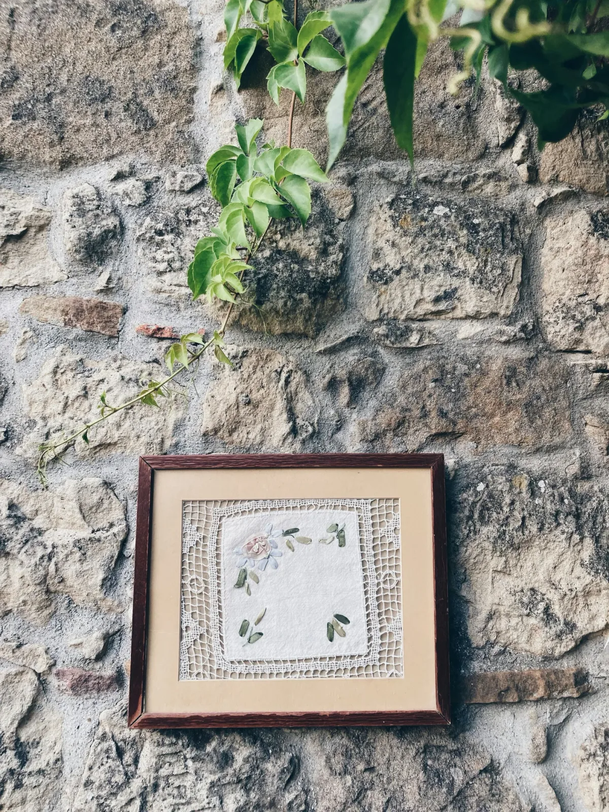 Broderie encadrée florale accrochée sur un mur en pierre, ambiance rustique champêtre