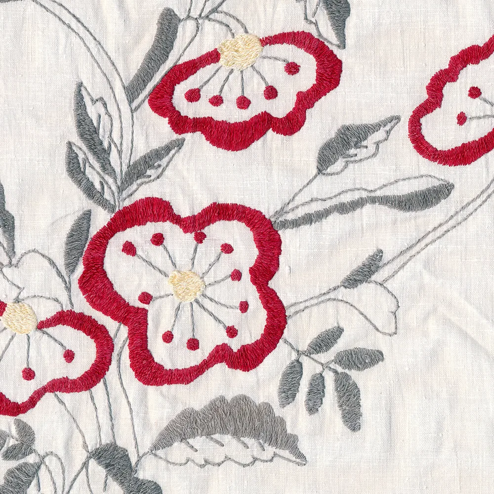 Détail de broderie florale au point de crewel sur lin blanc avec fleurs rouges et feuillages gris