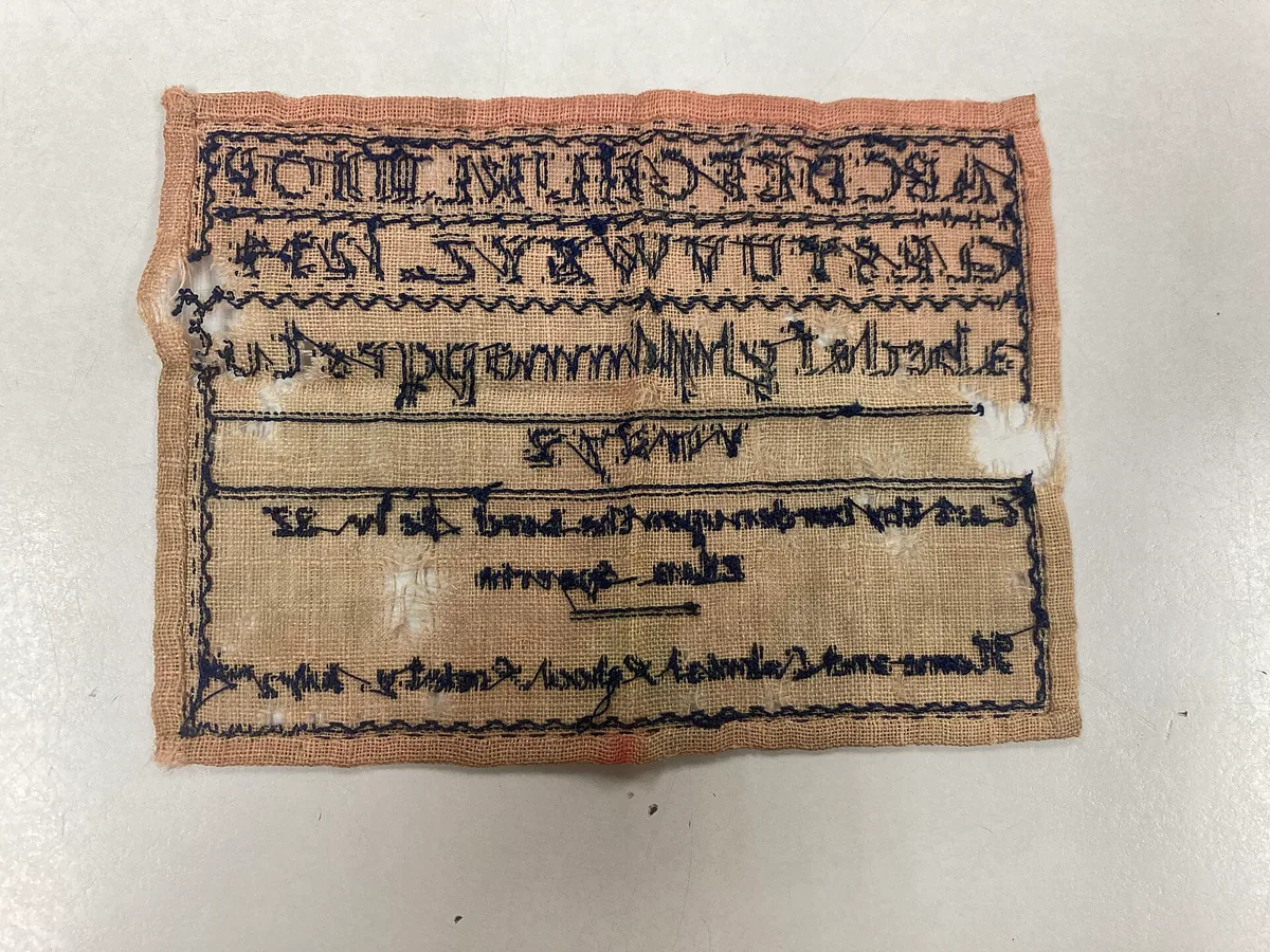 Envers d'un sampler du XIXe siècle où la signature et les alphabets brodés apparaissent en miroir