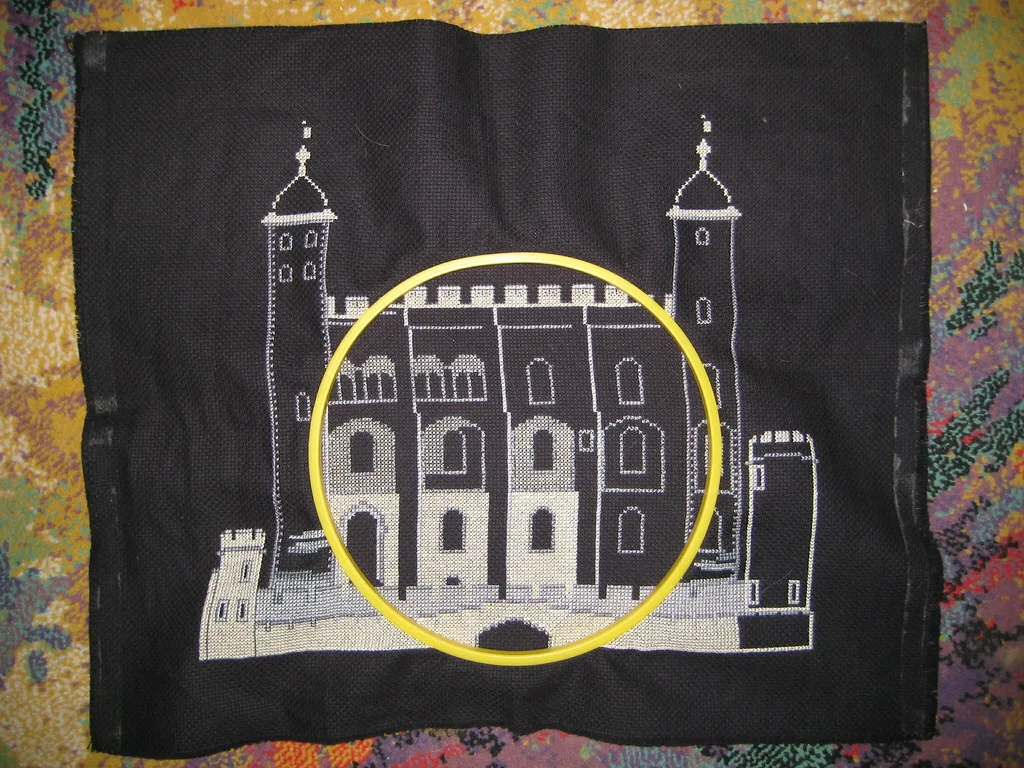 Broderie au point de croix en cours sur toile noire avec un cerceau jaune posé sur une zone du motif